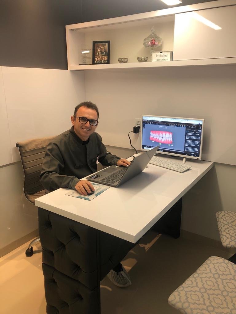 Dr. Rafael D'Avila sorrindo em seu consultório, ao lado da tela com o planejamento digital de um caso
