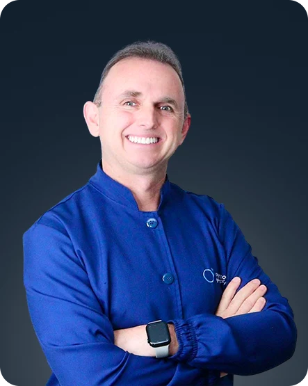 Dr. Rafael D'Avila sorrindo, de jaleco azul e braços cruzados