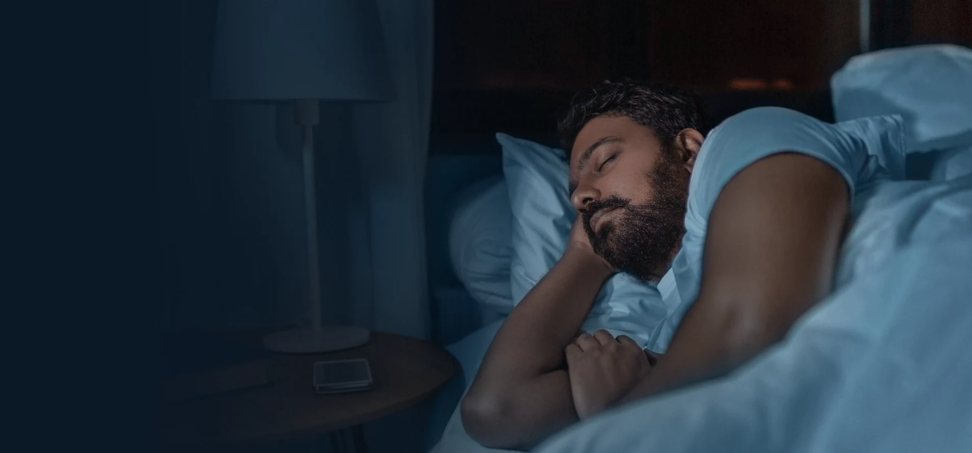 Homem dormindo à noite em seu quarto, com o abajur aceso ao lado da cama